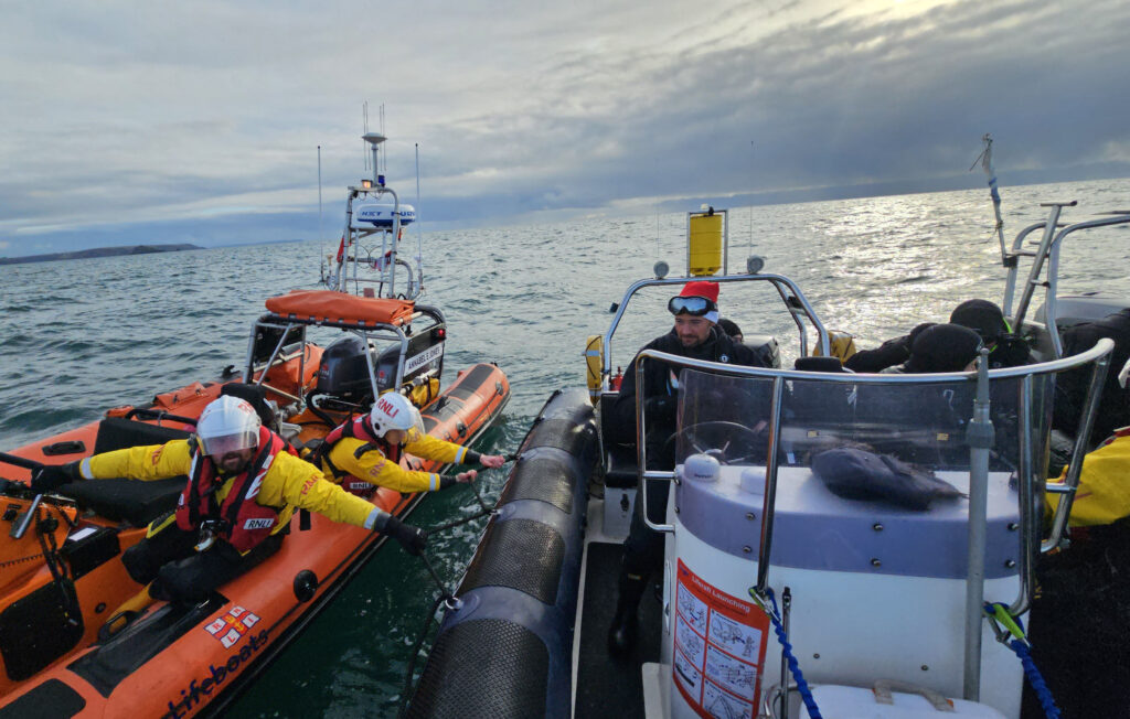 Plymouth ILB alongside PML Explorer with RNLI casualty care trained crew member onboard assessing the recovered diver.